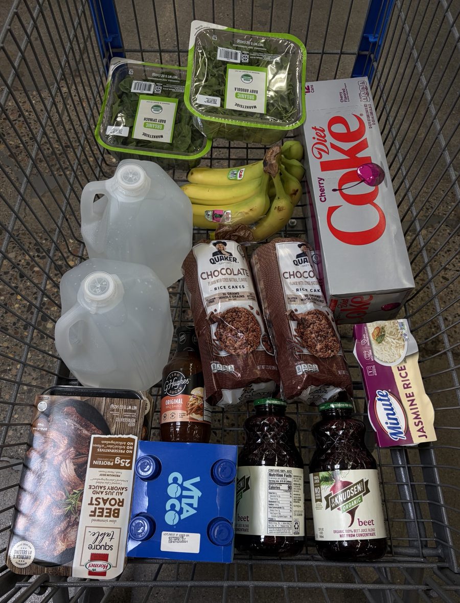 A shopping cart with greens, bananas, rice, rice cakes, water and juice